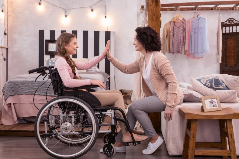 Disabled woman in wheelchair high fiving support worker at home