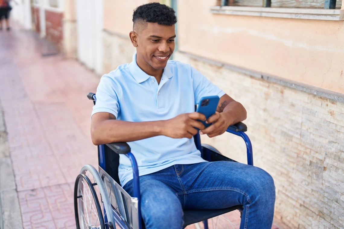 Disabled man in wheelchair smiling and using smartphone